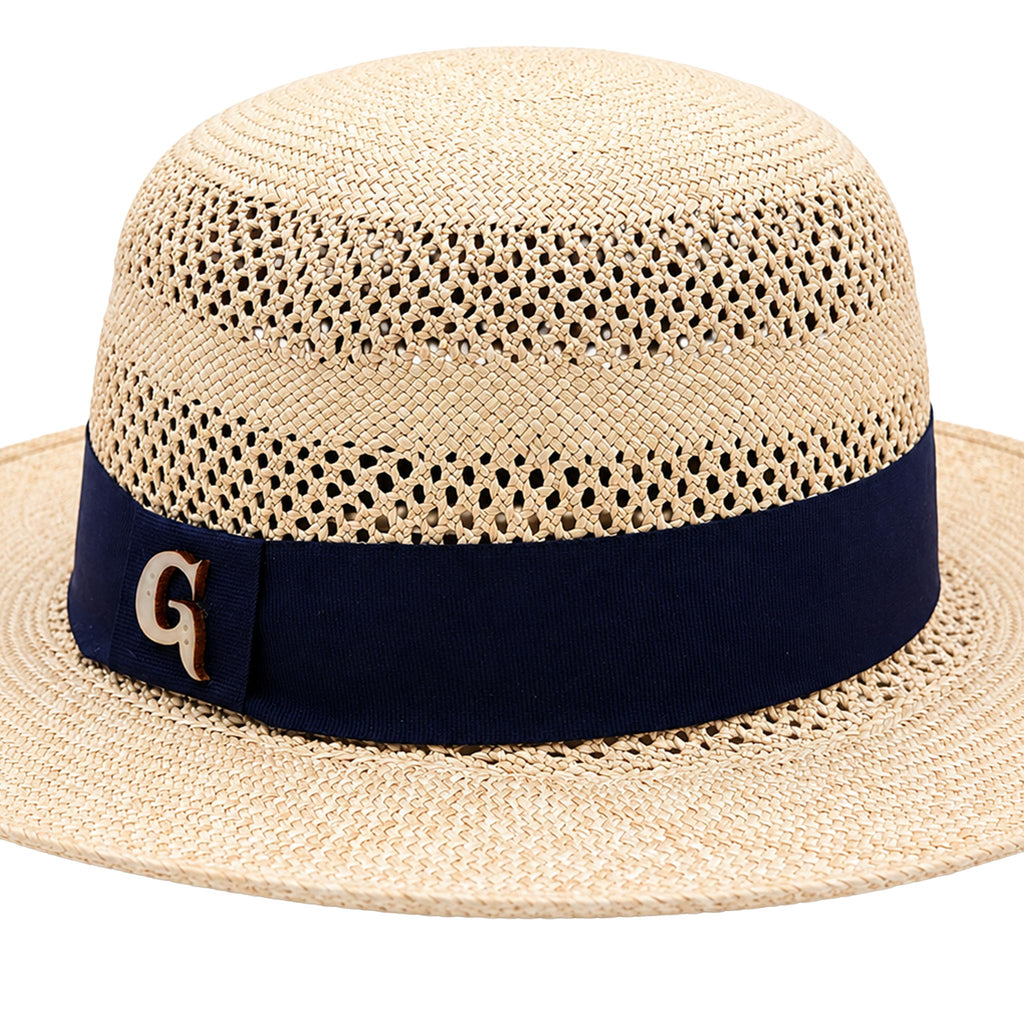 A light beige woven straw hat with a navy blue ribbon band and a gold letter 'G' accent on the side, shown against a plain white background.
